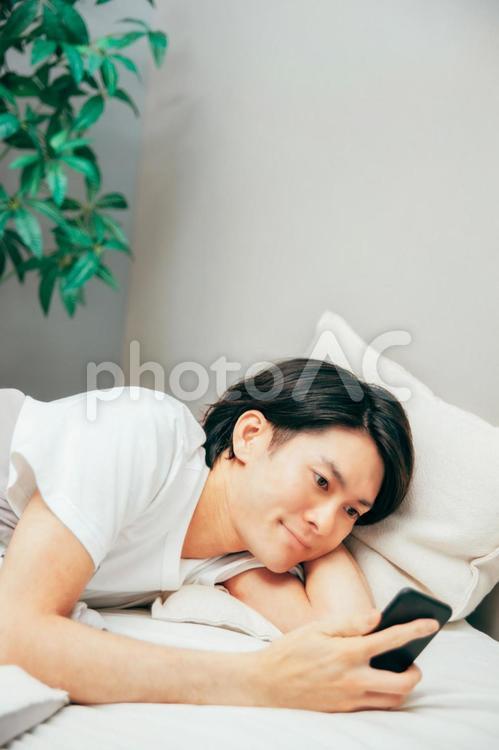 ベッドでスマホを見る男性（笑顔） スマートフォン,スマホ,アプリの写真素材