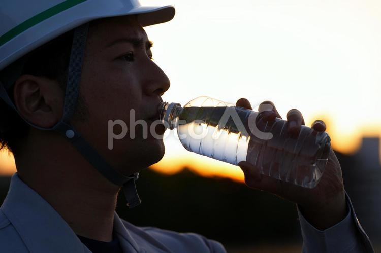 夕暮れ時に水を飲んでいる作業服の男性の横顔 男性,日本人,アジア人の写真素材