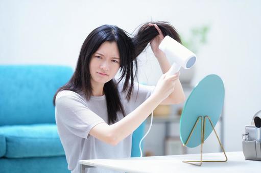 不機嫌な顔で髪を乾かしている女性 女性,ドライヤー,持つの写真素材