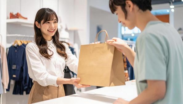 紙バックの商品を手渡す女性の店員の写真