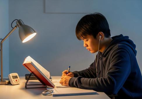 夜の机で集中して勉強する男子学生 夜の机で集中して勉強する男子学生の写真
