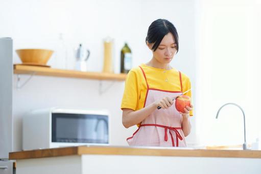 キッチンでリンゴの皮むきをしているエプロンの女性 女性,真剣,リンゴの写真素材