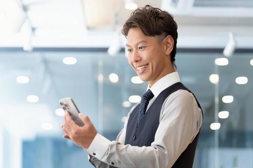 スマホの画面を見る笑顔の男性ビジネスマン スマホの画面を見る笑顔の男性ビジネスマン 男性,スマホ,スマートフォンの写真素材
