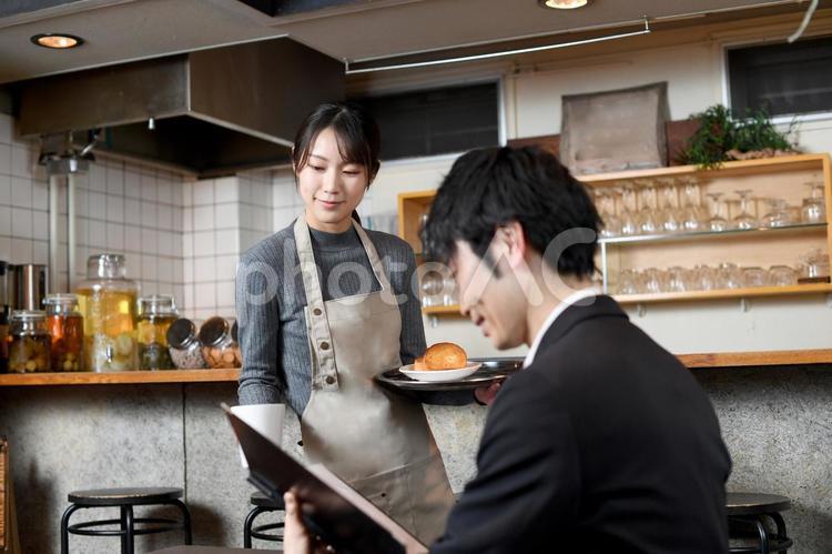 飲食店で男性客に食事の配膳をする女性店員 飲食店,レストラン,カフェの写真素材