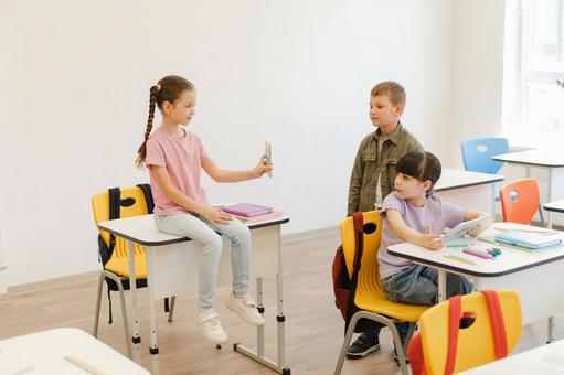 携帯を見せる女の子と振り向く生徒たち 男の子,女の子,子どもの写真素材