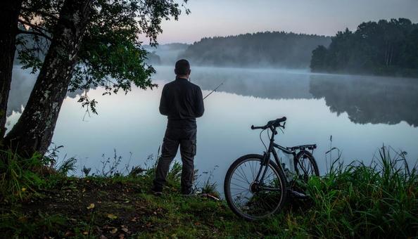 湖で釣りをする男性の後ろ姿と自転車 湖で釣りをする男性の後ろ姿と自転車の写真