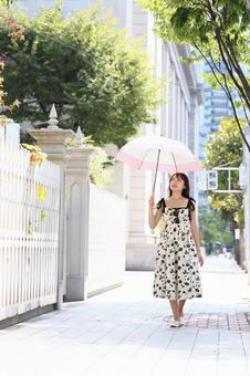 日傘をさして舗道を歩く女性 日傘をさして舗道を歩く女性の写真