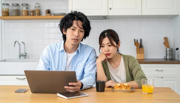 キッチンでパソコンを使い悩んでいる男女 キッチンでパソコンを使い悩んでいる男女の写真