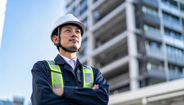 高層ビルの斜め上を見つめる若い作業服男性 高層ビルの斜め上を見つめる若い作業服男性の写真
