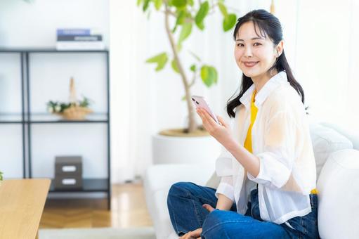 部屋でスマホを操作する女性 スマホ,笑顔,部屋の写真素材