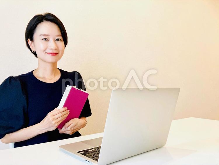 パソコンを使いながら本を手にする女性 女性,笑顔,本の写真素材