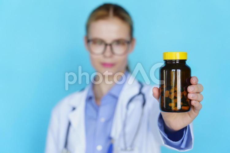 瓶の錠剤を見せるピンボケの女性 女性,メガネ,ロングヘアの写真素材
