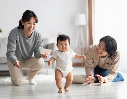 初めて歩いた赤ちゃんと見守る若い両親 初めて歩いた赤ちゃんと見守る若い両親の写真