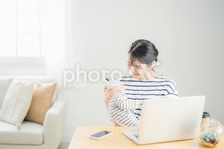 赤ちゃんを抱きながらパソコンを使う女性 育児休業,パソコン,在宅勤務の写真素材