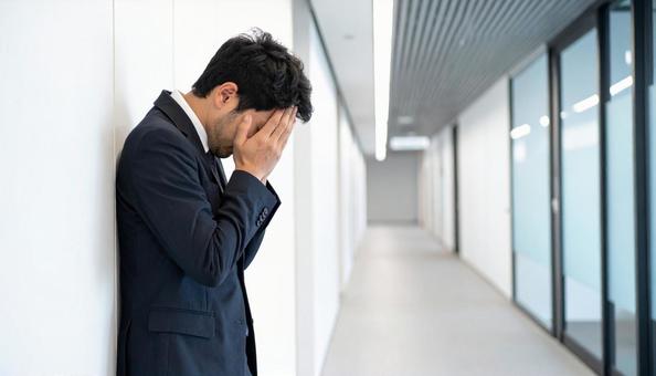 オフィスビルの廊下で苦悩するビジネスマンの写真