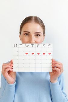 月経期間を示すカレンダーを手に持ったカメラ目線の女性（白背景） 生理,月経,女性の写真素材