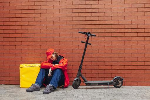 電動キックボードのそばに座り込む男性配達員 配達,フードデリバリー,デリバリーの写真素材