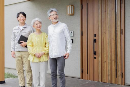 住宅の前で笑う男性作業員とシニア夫婦 住宅の前で笑う男性作業員とシニア夫婦 シニア,夫婦,見上げるの写真素材