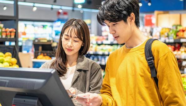 スーパーでセルフレジを使う若い日本人夫婦 スーパーでセルフレジを使う若い日本人夫婦の写真