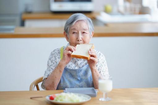 食パンを食べているエプロン姿の高齢女性 女性,食パン,持つの写真素材