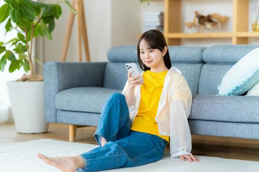 部屋でスマホを操作する若い女性 部屋でスマホを操作する若い女性 スマホ,若い女性,笑顔の写真素材