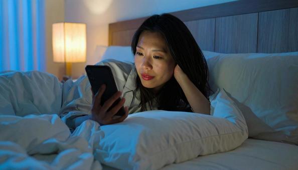ベッドルームでスマホを見る日本人女性 ベッドルームでスマホを見る日本人女性の写真