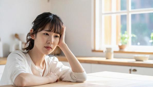 疲れた表情でキッチンに座る若い女性 疲れた表情でキッチンに座る若い女性の写真