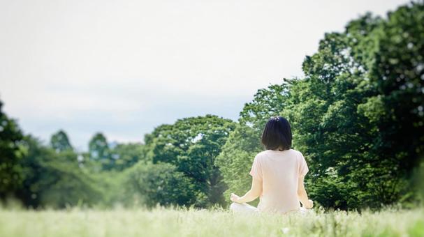A woman meditating on a natural lawn A woman meditating on a natural lawn