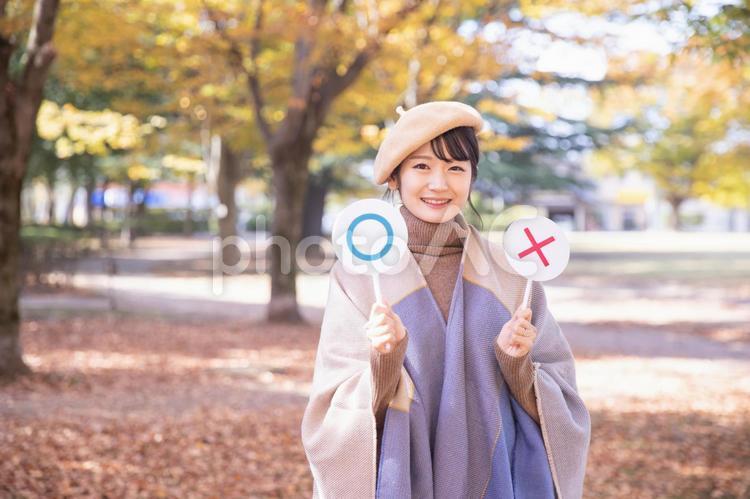 秋の公園でマルバツを持つ女性（笑顔） 選ぶ,選択,バツの写真素材