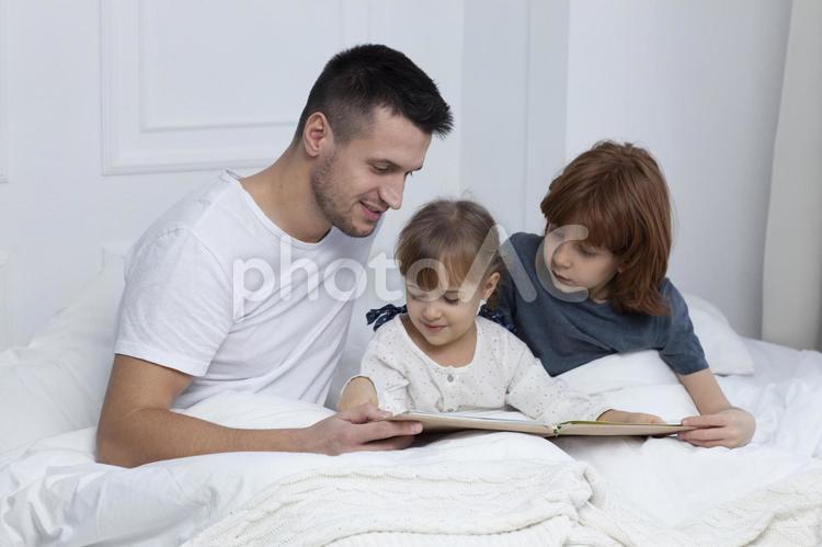 ベッドで絵本を読むお父さんと子どもたち3 お父さん,外国人,親子の写真素材