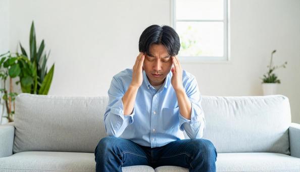 ソファに座って頭を抱える20代の男性の写真