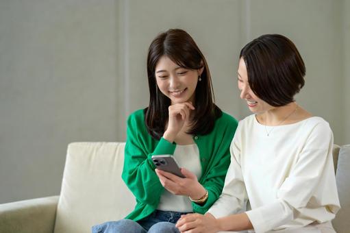 ソファに座って笑い合う日本人女性 ソファに座って笑い合う日本人女性 おしゃべり,リビング,友達の写真素材