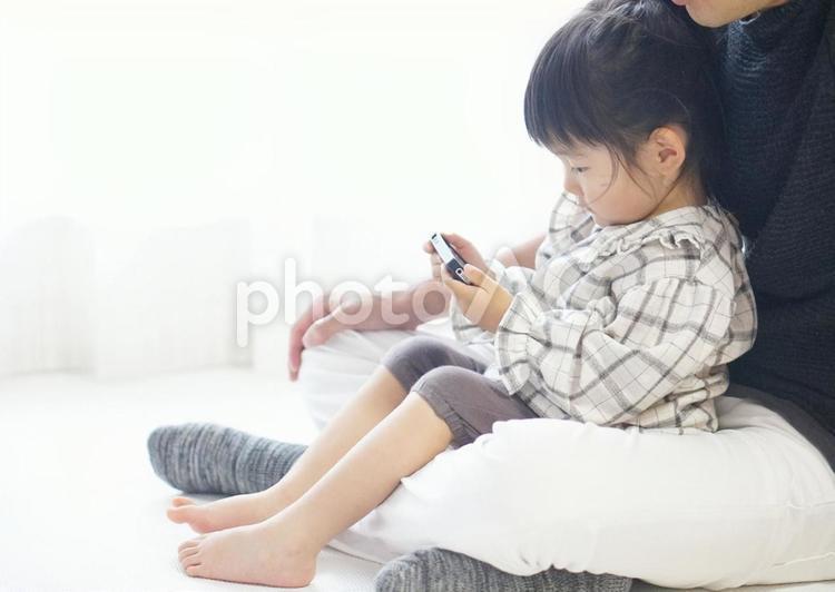 父の膝の上でスマホを観る女の子 スマホ,動画,父と娘の写真素材