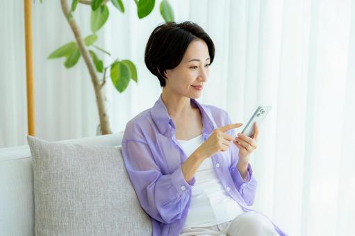 部屋でスマホを使うミドル女性 スマホ,笑顔,女性の写真素材
