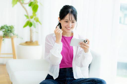 部屋でスマホを操作する若い女性 スマホ,笑顔,若い女性の写真素材