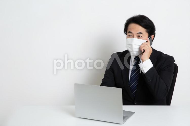 マスクをしながら電話をしている中年のサラリーマン男性（コピースペース） 中年,上司,会社員の写真素材