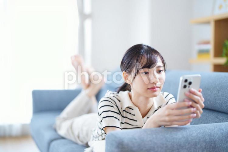 ソファでスマホを見て寛ぐ女性 女性,スマートフォン,持つの写真素材