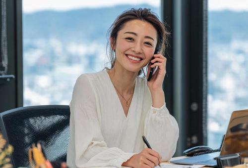 仕事をしながら笑顔で電話をする女性の写真