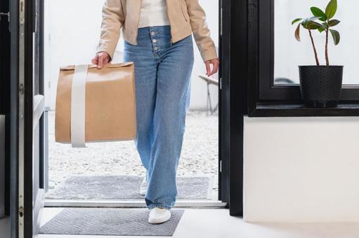 置き配された紙袋を持って家に入る女性 配達,フードデリバリー,デリバリーの写真素材