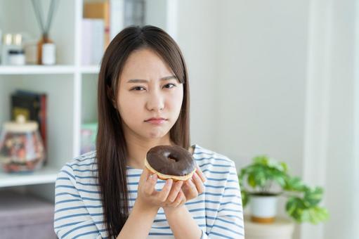 ダイエットで悩む若い女性 ダイエットで悩む若い女性 悩む,ドーナツ,ダイエットの写真素材