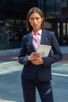 オフィスビルの外でタブレットを持って立つパンツスーツのアジア人ビジネスウーマン ビジネスウーマン,ビジネス,女性の写真素材