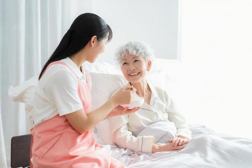 寝ているシニア女性を介護をする介護士 寝ているシニア女性を介護をする介護士 食事,介護,介護士の写真素材