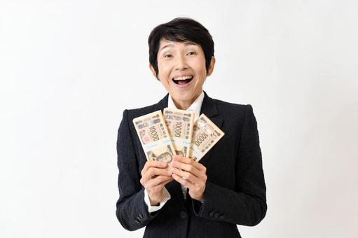 札束を持ち驚くスーツ姿の笑顔のミドル女性 ミドル女性,お金,札束の写真素材
