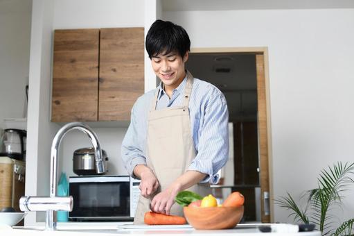 A young black-haired man in an apron cooking in the kitchen, un uomo, cucina, una cucina, JPG