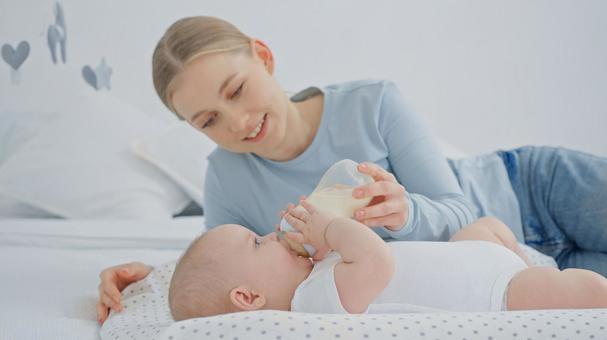 ミルクを飲んでいる横向きの赤ちゃんを見つめる女性 ミルクを飲んでいる横向きの赤ちゃんを見つめる女性 赤ちゃん,哺乳瓶,飲むの写真素材