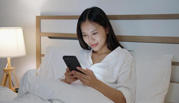 ベッドルームでスマホを見る日本人女性 ベッドルームでスマホを見る日本人女性の写真