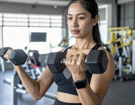 ジムでダンベル筋トレする女性 ジムでダンベル筋トレする女性の写真
