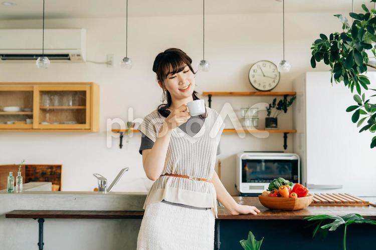 キッチンの前でホットドリンクを飲む女性 コーヒー,女性,お茶の写真素材