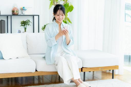 部屋でスマホを操作する若い女性 スマホ,笑顔,女性の写真素材