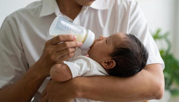 椅子に座り赤ちゃんに哺乳瓶で授乳する父親 椅子に座り赤ちゃんに哺乳瓶で授乳する父親の写真